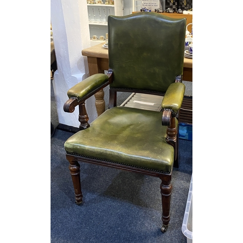 552 - A green leather upholstered armchair with arched back, open padded arms, on baluster legs and castor... 