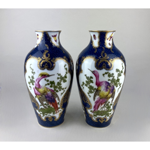 443 - A pair of porcelain vases decorated with exotic birds in a landscape inside gilt frames against a sc... 