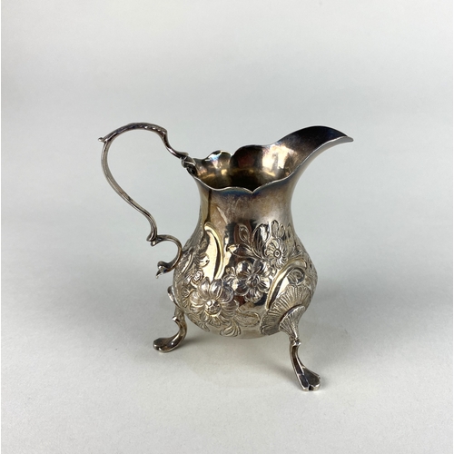 73 - A George IV silver cream jug with scroll handle and later embossed floral decoration, on three feet,... 