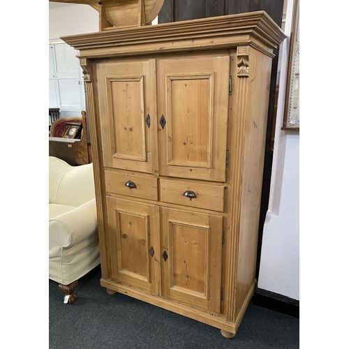 922 - A vintage pine cupboard with moulded pediment over two panel doors enclosing shelves over a pair of ... 
