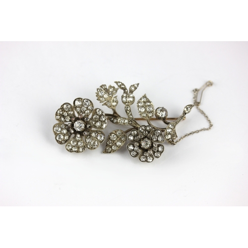 145 - A gold-backed and silver set diamond brooch designed as a floral and foliate spray, the two flower h... 