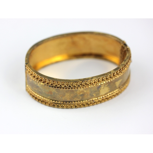 51 - A Victorian gold oval hinged bangle with applied decoration to the front border, on a snap clasp, un... 