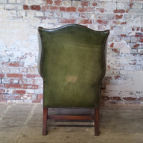 67 - An early 20th century green leather wing back arm chair, stud work, H-frame stretcher