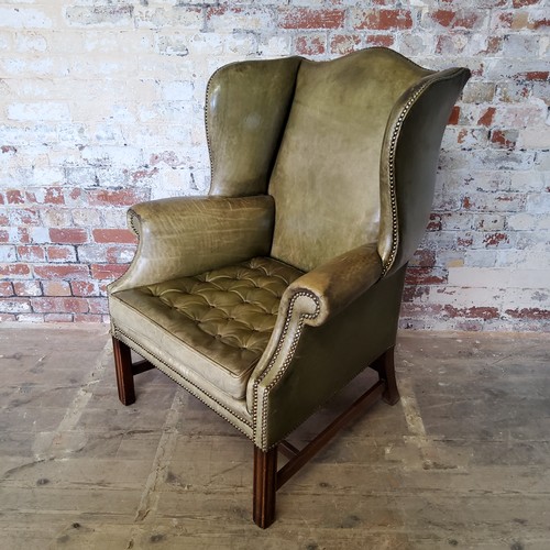 67 - An early 20th century green leather wing back arm chair, stud work, H-frame stretcher