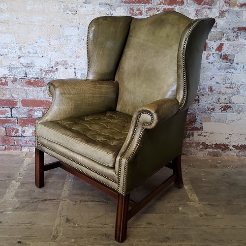 67 - An early 20th century green leather wing back arm chair, stud work, H-frame stretcher