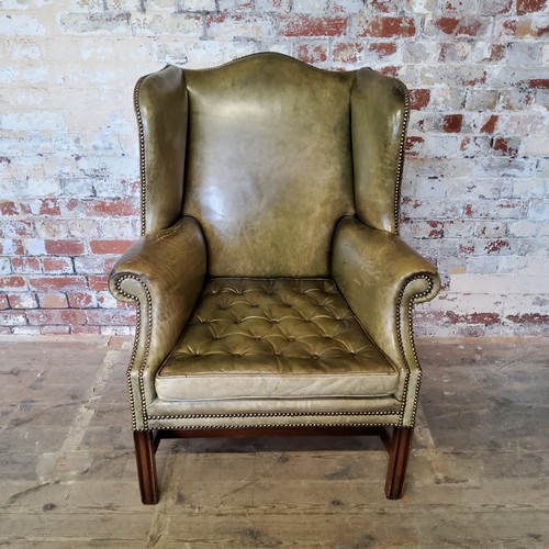 67 - An early 20th century green leather wing back arm chair, stud work, H-frame stretcher