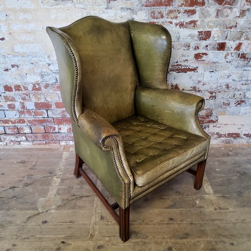 67 - An early 20th century green leather wing back arm chair, stud work, H-frame stretcher