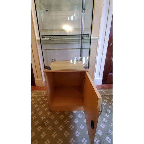 249 - A contemporary locking glazed display unit, enclosing three glass shelves on a beech veneered cupboa... 