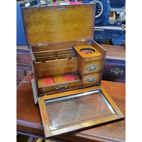 60 - An early 20th century oak stationery box, the hinged top releases the glazed fall front revealing a ... 