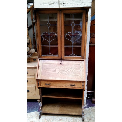 36 - An Arts & Crafts oak bureau bookcase with oversailing cornice, sinuous stained glass leaded pane... 