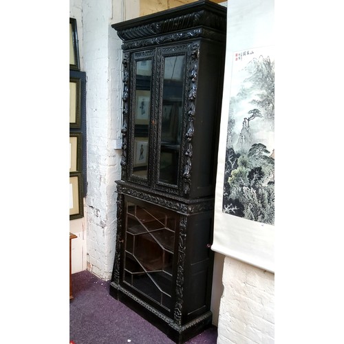 45 - A tall Victorian ebonised display cabinet, comprising of heavily carved with masks, scrolls and flow... 