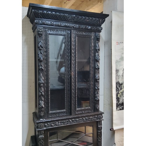 45 - A tall Victorian ebonised display cabinet, comprising of heavily carved with masks, scrolls and flow... 