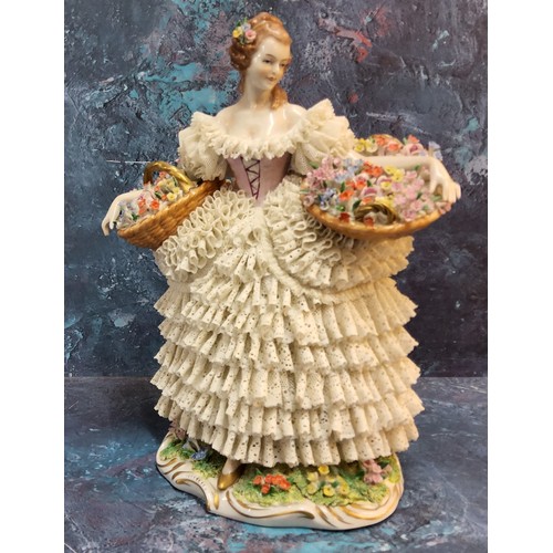 326 - A Sitzendorf lace figure, of a Flower Lady, she stands holding with two baskets, her skirt from dipp... 