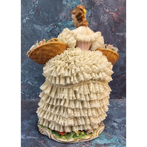 326 - A Sitzendorf lace figure, of a Flower Lady, she stands holding with two baskets, her skirt from dipp... 