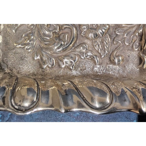 91 - An Edwardian silver card tray, fluted border, heavily embossed with scroll & foliate, vacant cen... 