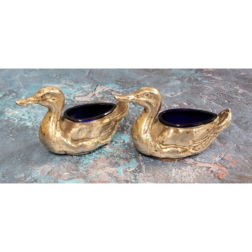 130 - A pair of Edwardian novelty silver salts, as ducks, blue glass liners, 9.5cm wide, Birmingham 1906