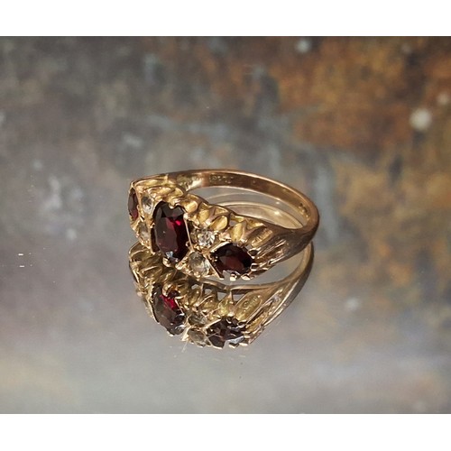 92 - A 9ct gold garnet and diamond gypsy ring, the central oval garnet flanked by two round garnets inter... 