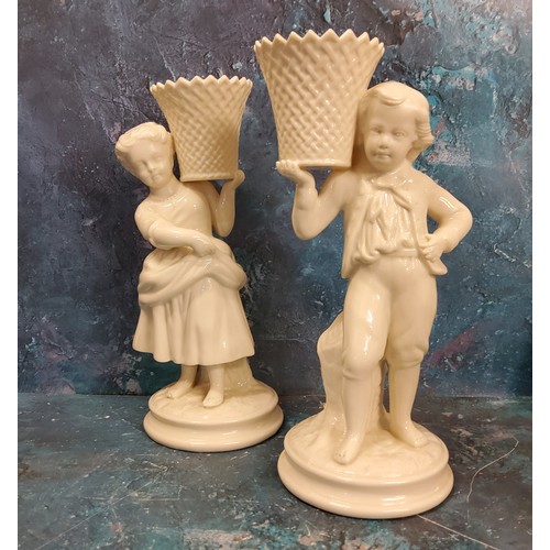 6 - A pair of Belleek figural spill vases, modelled as a boy and a girl  holding baskets, 21.5cm high, b... 