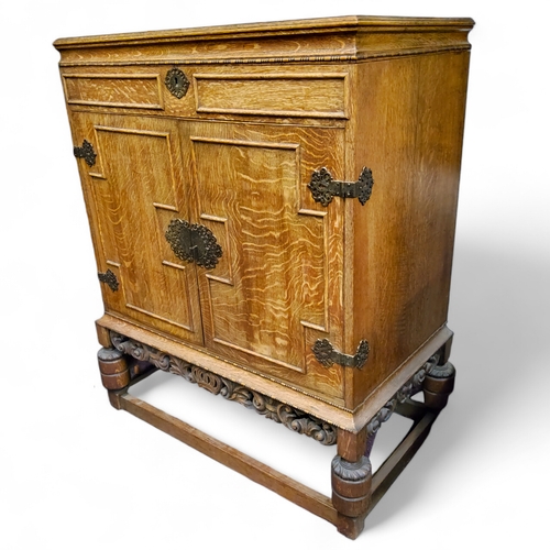 113 - An early 20th century golden oak cabinet, the hinged top revealing niche, above two fielded panelled... 