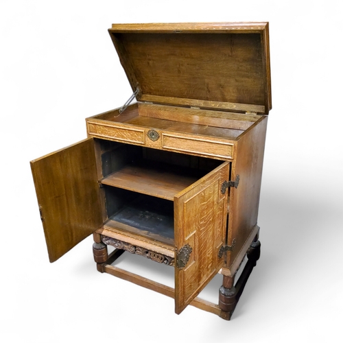 113 - An early 20th century golden oak cabinet, the hinged top revealing niche, above two fielded panelled... 