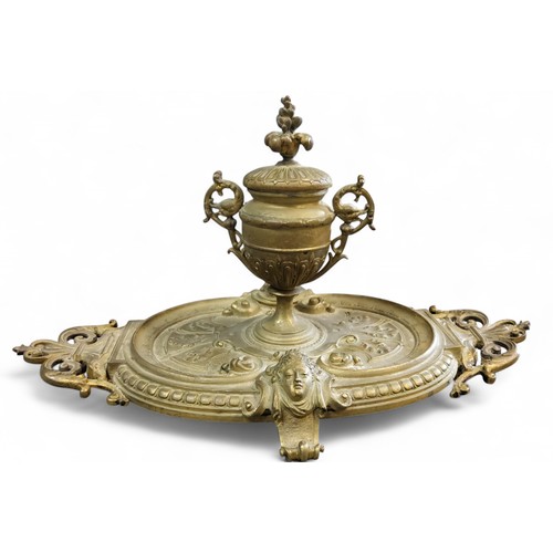 393 - A Victorian bronzed standish, with pedestal two handled urnular well, leafy finial, the oval stand c... 