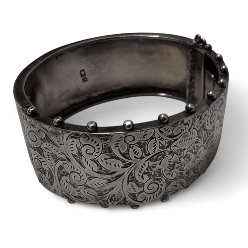218 - A Victorian silver hinged bangle, engraved and chased with foliate scrolls and L H Februrary 5th 188... 
