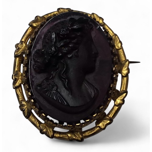 226 - A Victorian gilt metal oval brooch, the central purple glass panel depicting a classical lady in rel... 