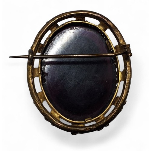 226 - A Victorian gilt metal oval brooch, the central purple glass panel depicting a classical lady in rel... 