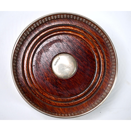 19 - A modern pierced silver bottle coaster, the turned wood base inset with silver button, 13cm diameter... 