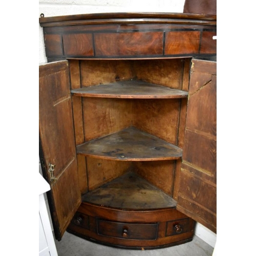 582 - A 19th century mahogany hanging corner cupboard with two doors enclosing shelves over central drawer... 