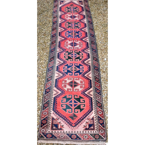 627 - A Caucasian geometric design red ground runner with brown border, 310 x 80 cm