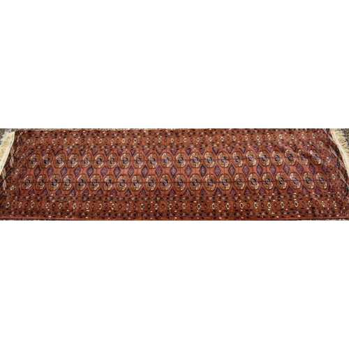 507 - A contemporary Turkoman design rug, the repeating gul design on rust-red ground, 270 cm x 83 cm