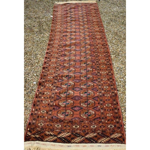 507 - A contemporary Turkoman design rug, the repeating gul design on rust-red ground, 270 cm x 83 cm