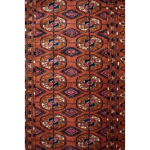 507 - A contemporary Turkoman design rug, the repeating gul design on rust-red ground, 270 cm x 83 cm