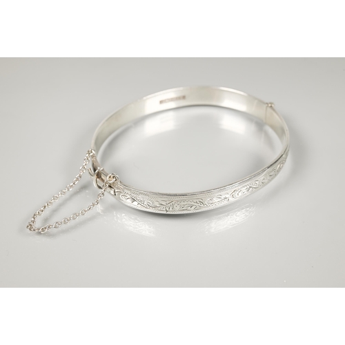 202 - A silver oval half-hinged bangle with engraved foliate decoration, safety chain attached; on Italian... 