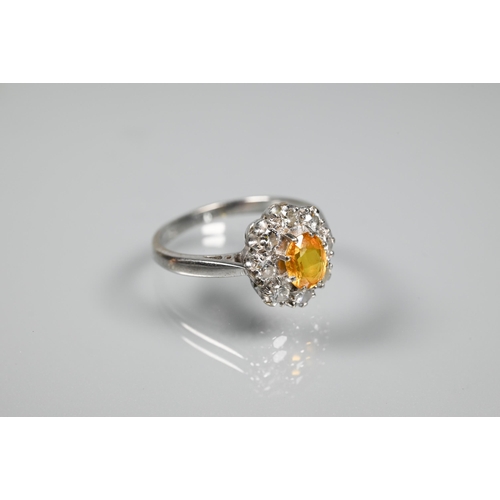 228 - An oval cluster ring set with oval yellow sapphire (?), surrounded by nine diamonds, white metal sta... 