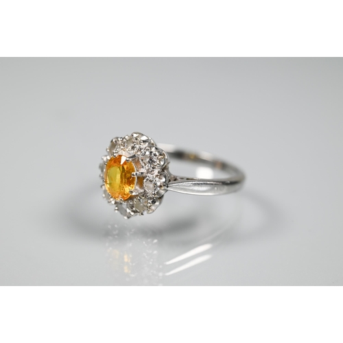 228 - An oval cluster ring set with oval yellow sapphire (?), surrounded by nine diamonds, white metal sta... 