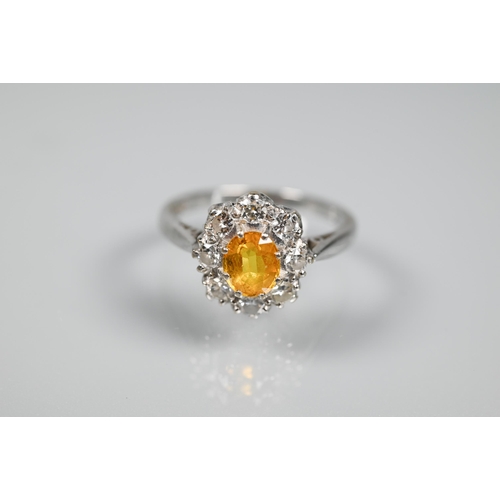 228 - An oval cluster ring set with oval yellow sapphire (?), surrounded by nine diamonds, white metal sta... 