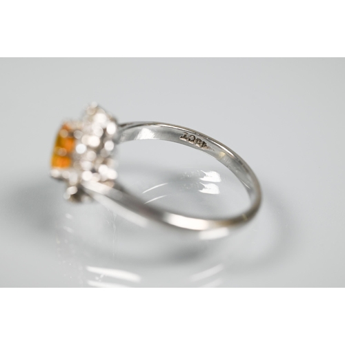 228 - An oval cluster ring set with oval yellow sapphire (?), surrounded by nine diamonds, white metal sta... 