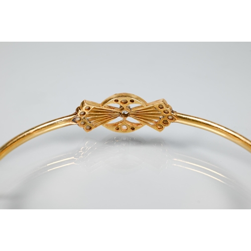 257 - A yellow gold oval half-hinged bangle of simple form with seed pearl and diamond stylised bow to cen... 