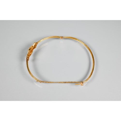 257 - A yellow gold oval half-hinged bangle of simple form with seed pearl and diamond stylised bow to cen... 