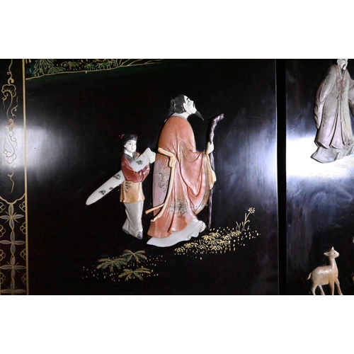 327A - An early 20th century Chinese lacquered four panel screen painted and gilded with idyllic landscapes... 