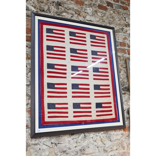 964 - A small vintage quilt, worked with stylised United States flags, 83 x 66 cm, mounted, framed and gla... 