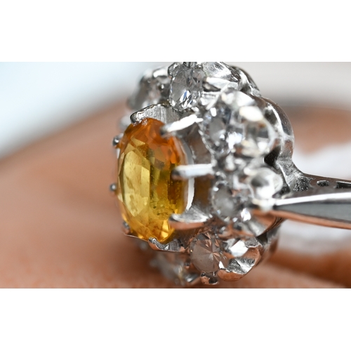 228 - An oval cluster ring set with oval yellow sapphire (?), surrounded by nine diamonds, white metal sta... 