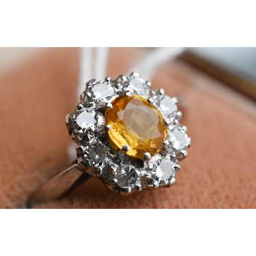 228 - An oval cluster ring set with oval yellow sapphire (?), surrounded by nine diamonds, white metal sta... 