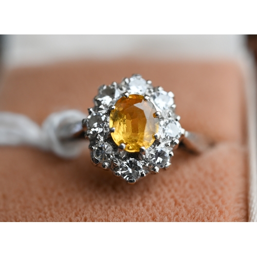 228 - An oval cluster ring set with oval yellow sapphire (?), surrounded by nine diamonds, white metal sta... 