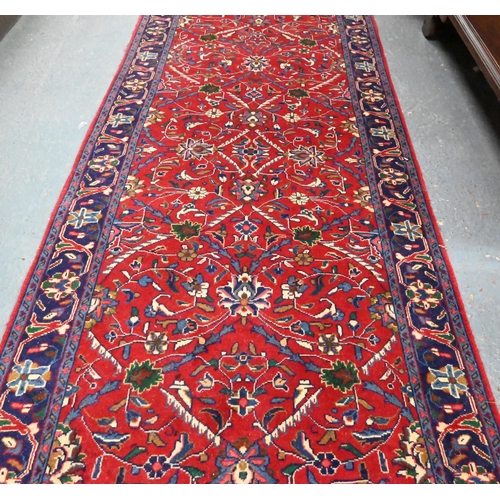 918 - A Persian Sarouk runner, the red ground with repeating design of interlinked floral vines, 307 cm x ... 