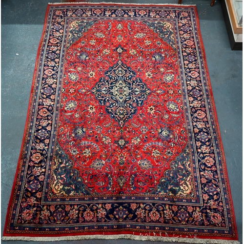 923 - A Persian Sarouk carpet, the red ground centred by a blue ground medallion radiating floral vines, 3... 