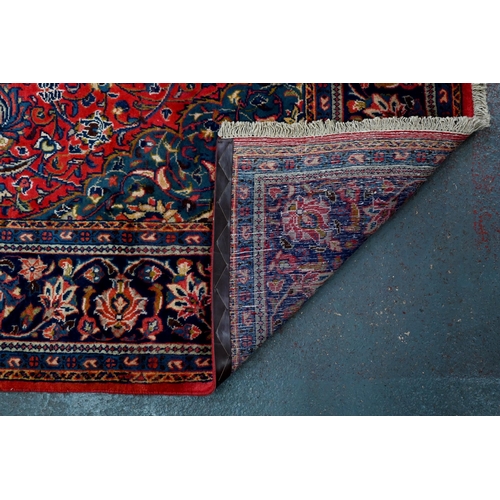 923 - A Persian Sarouk carpet, the red ground centred by a blue ground medallion radiating floral vines, 3... 