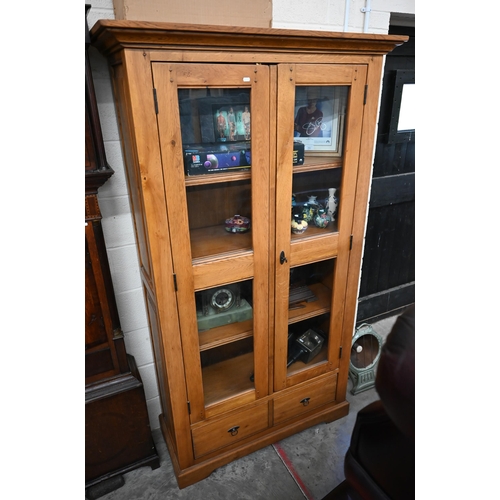 493 - A pale oak two door glazed shelving unit with four shelves and one drawer below, 110 cm wide x 194 c... 